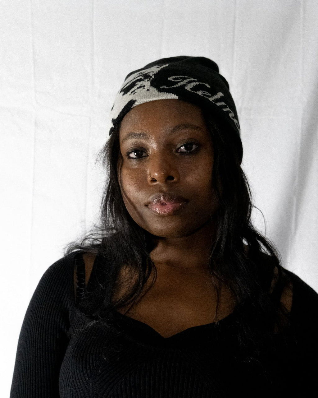 Woman wearing a black Helmet of Salvation beanie with white text against a white background