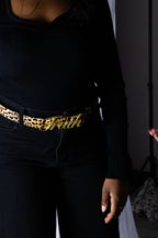 Person wearing a black outfit with a gold 'Truth' belt and leopard print details.