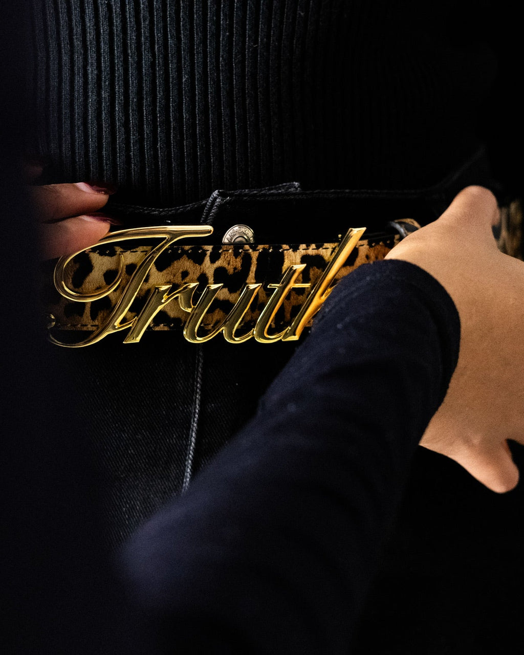 Gold belt with 'TRUTH' buckle leopard belt strap worn by a person against a dark background