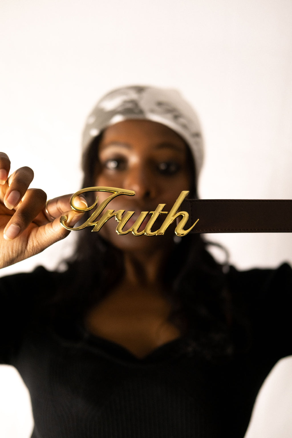 Person holding a gold 'Truth' buckle against a white background. LOVE GOD BIG Christian streetwear clothing brand. New Zealand Faith-based apparel.