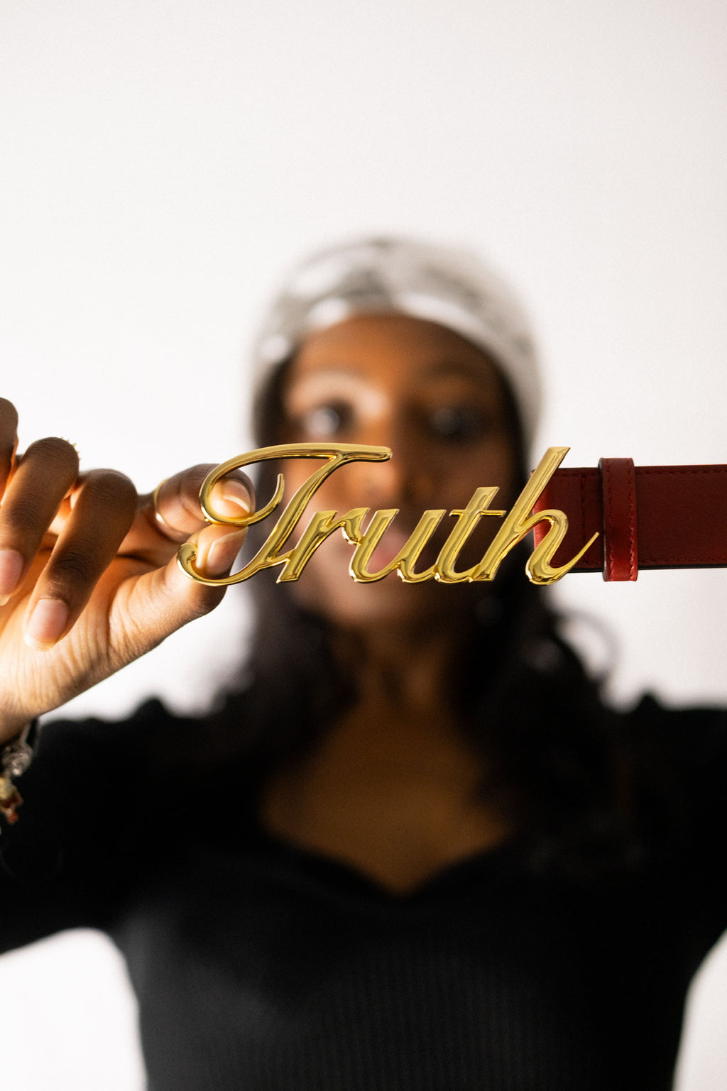 Person holding a gold 'Truth' belt buckle against a white background. Belt of Truth in Red - Christian Belt. LOVE GOD BIG Christian streetwear clothing brand. New Zealand Faith-based apparel.
