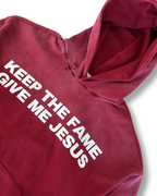 Red hoodie with white text 'KEEP THE FAME GIVE ME JESUS' on a white background