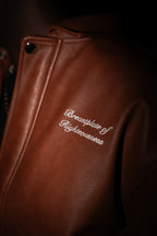 Brown leather jacket with embroidered text on a dark background. LOVE GOD BIG. CHRISTIAN CLOTHING BRAND