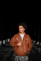 Man wearing a brown Breastplate of Righteousness leather jacket in a dark forest setting. LOVE GOD BIG Christian clothing brand streetwear faith-based apparel.